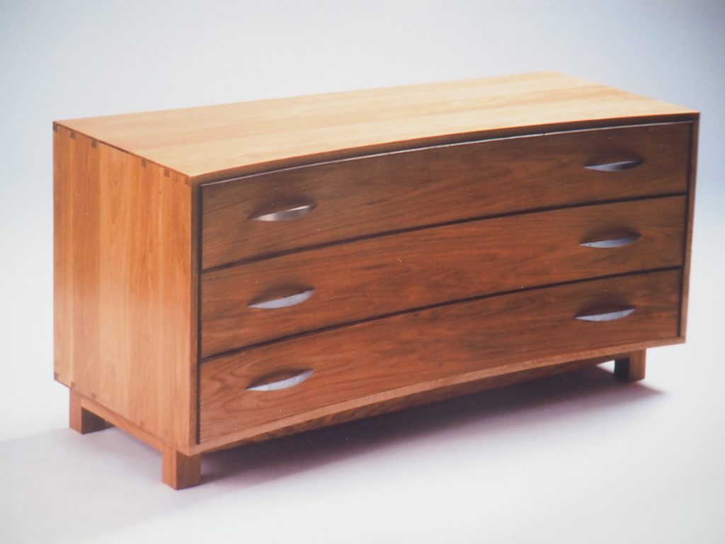 Concave chest of drawers with lipped dovetail construction. Made in chestnut with walnut cock-beading. Three dovetailed drawers with cedar bottoms finish of this timeless peace of furniture.